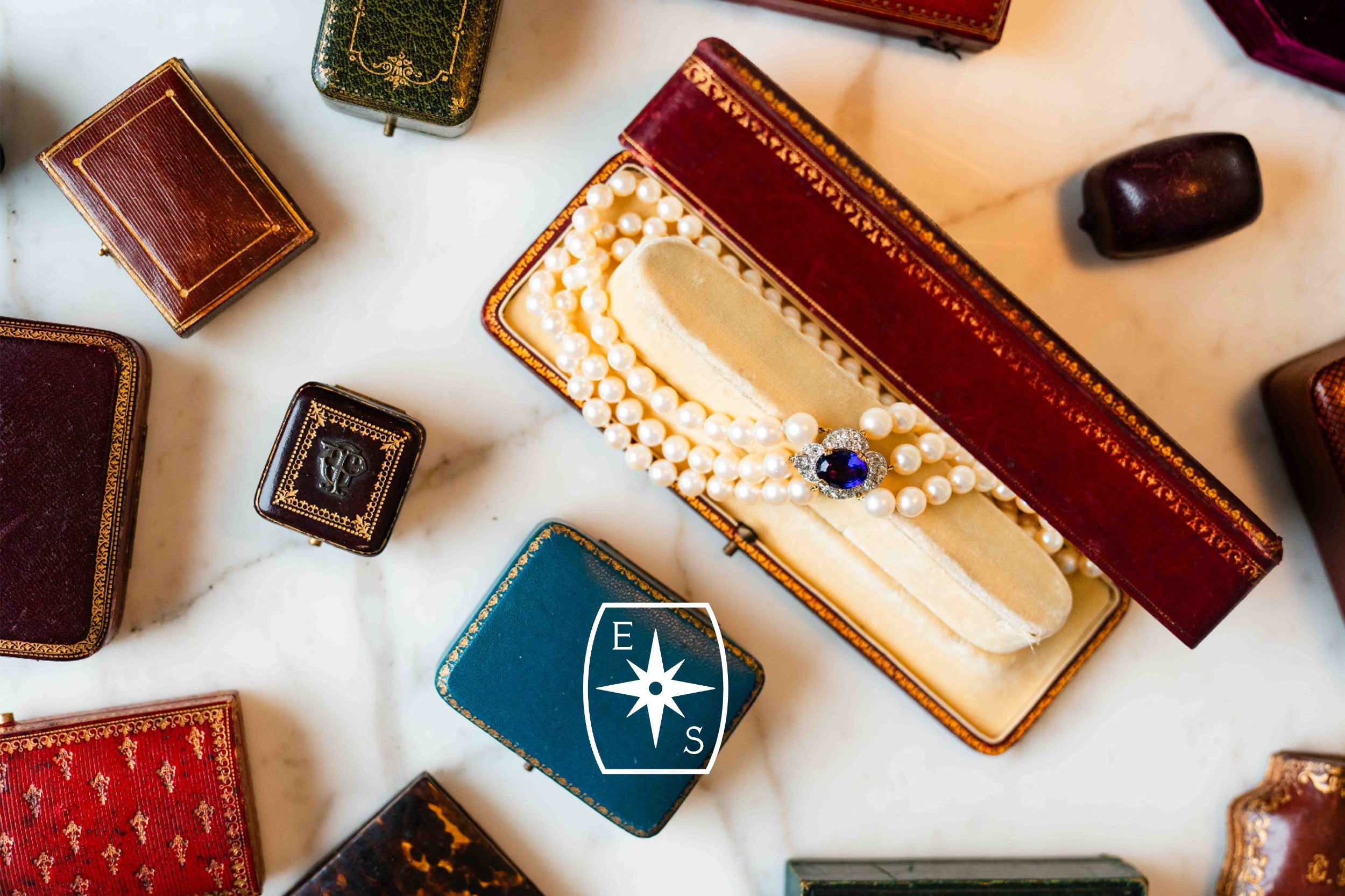 Collection of vintage jewelry boxes with a prominent one open to reveal pearls and a brooch.